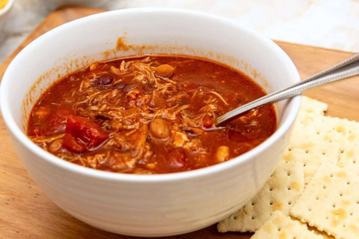Pulled pork chili in white bowl with silver spoon.