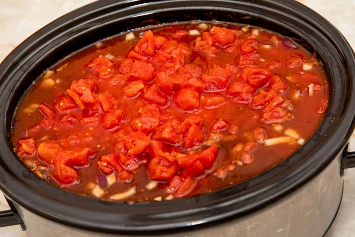 Slow cooker filled to the top with diced tomatoes and chili ingredients.