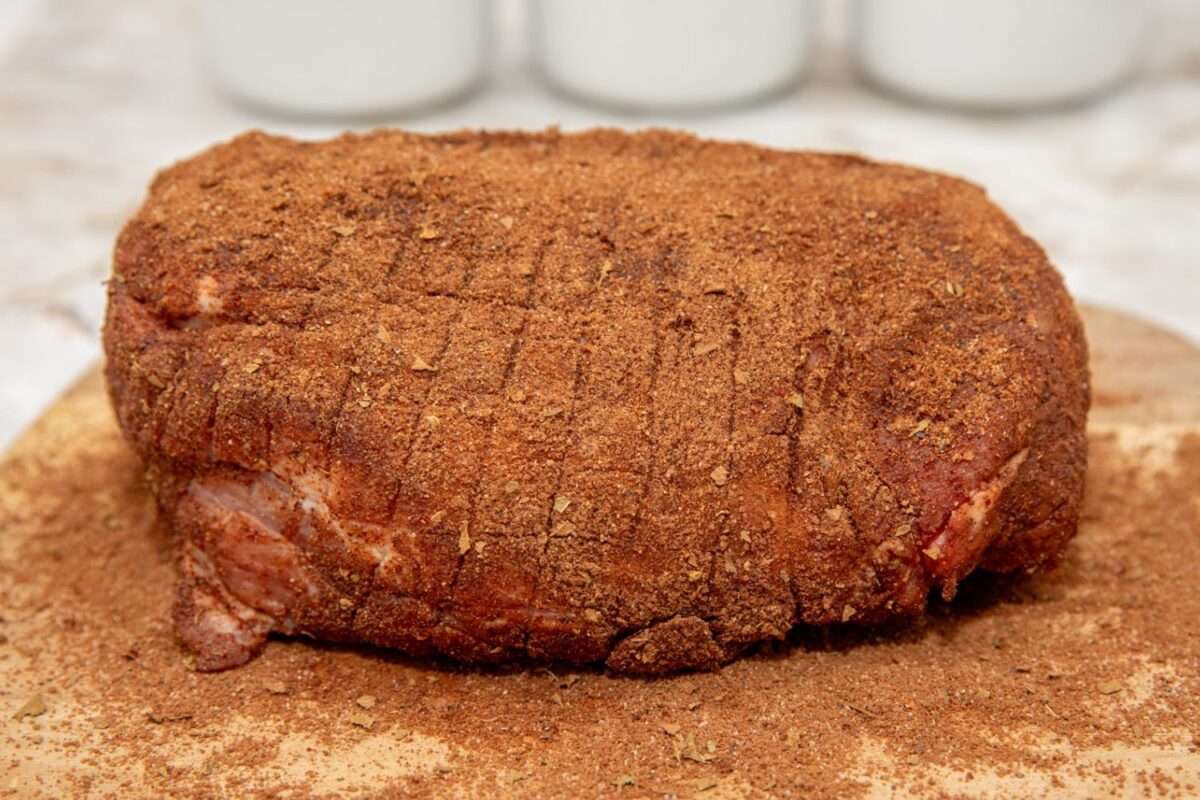 Pork shoulder covered with dry rub and resting on cutting board.