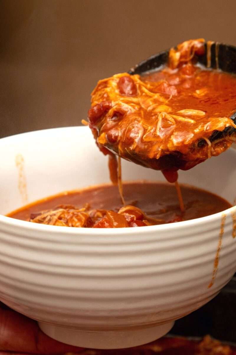 Vertical shot of pulled pork chili pouring out of black ladle.