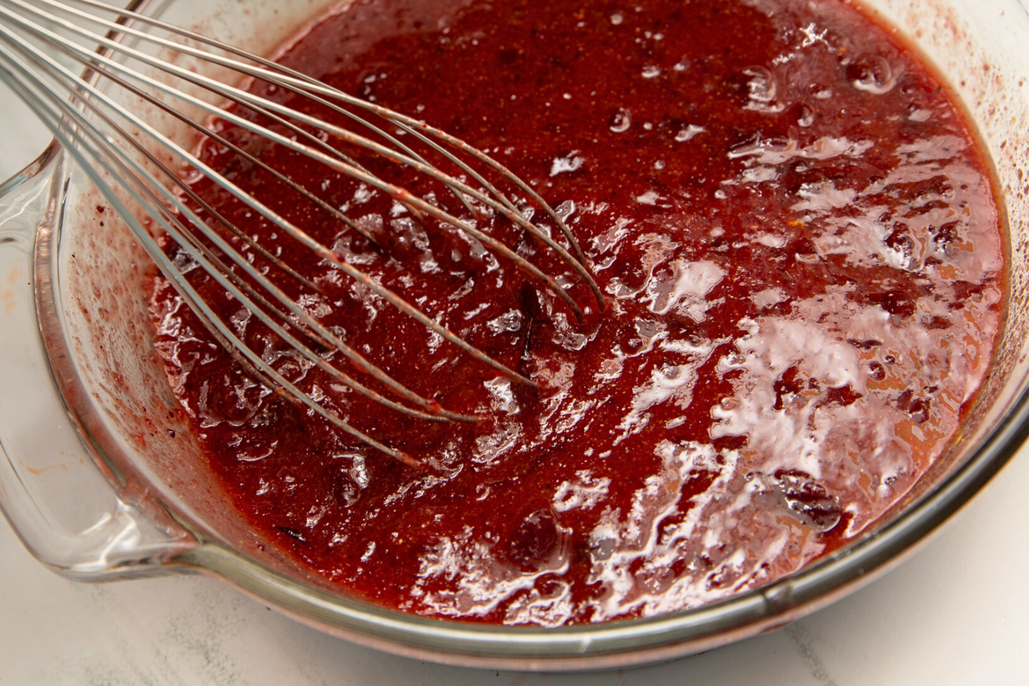 Wire whisk in glass bowl of cranberry sauce mixture.