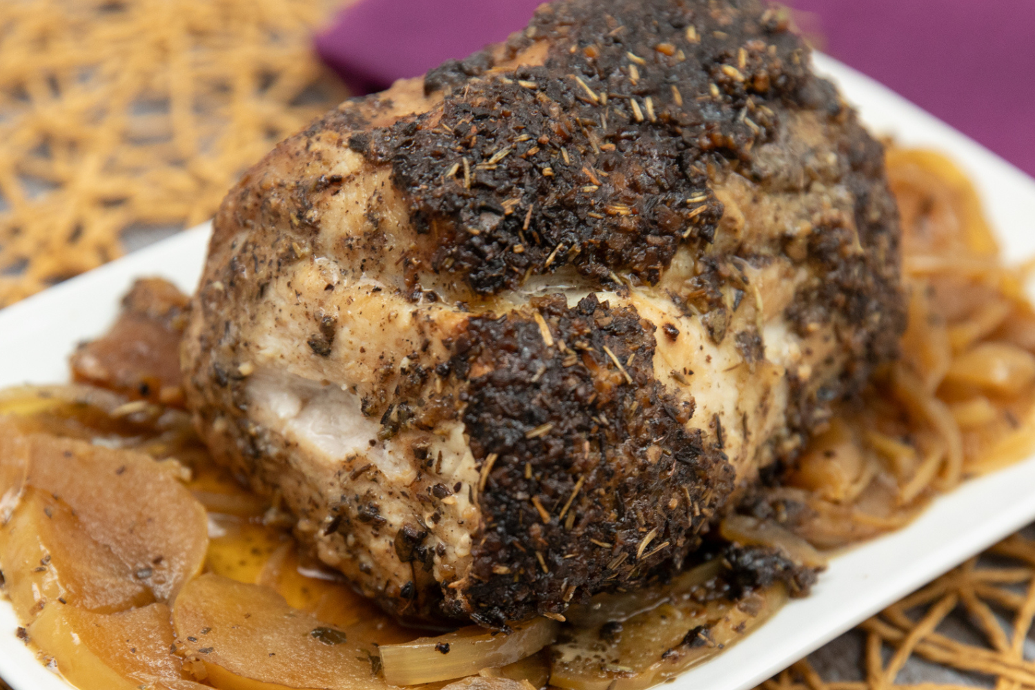 Ready to eat pork ribeye roast with onions and apples on a white plate and a seasoning crust. 