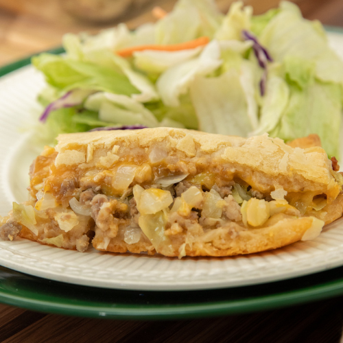 A slice of bierock casserole on a plate with salad behind it.