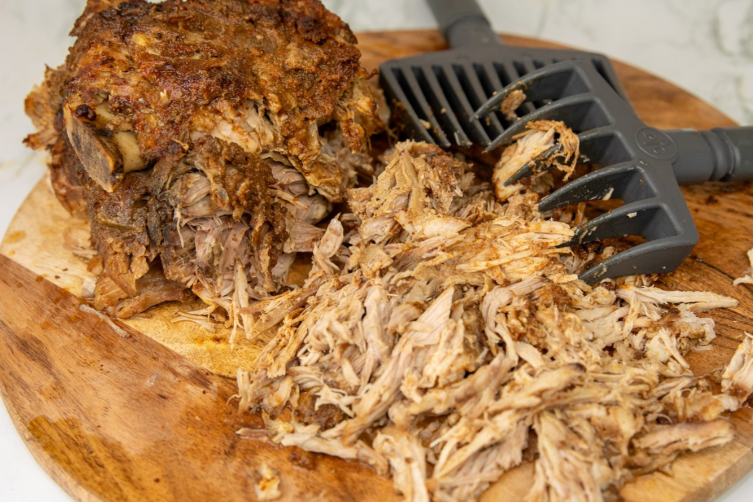 Pulled pork on wooden cutting board with black shredding forks.