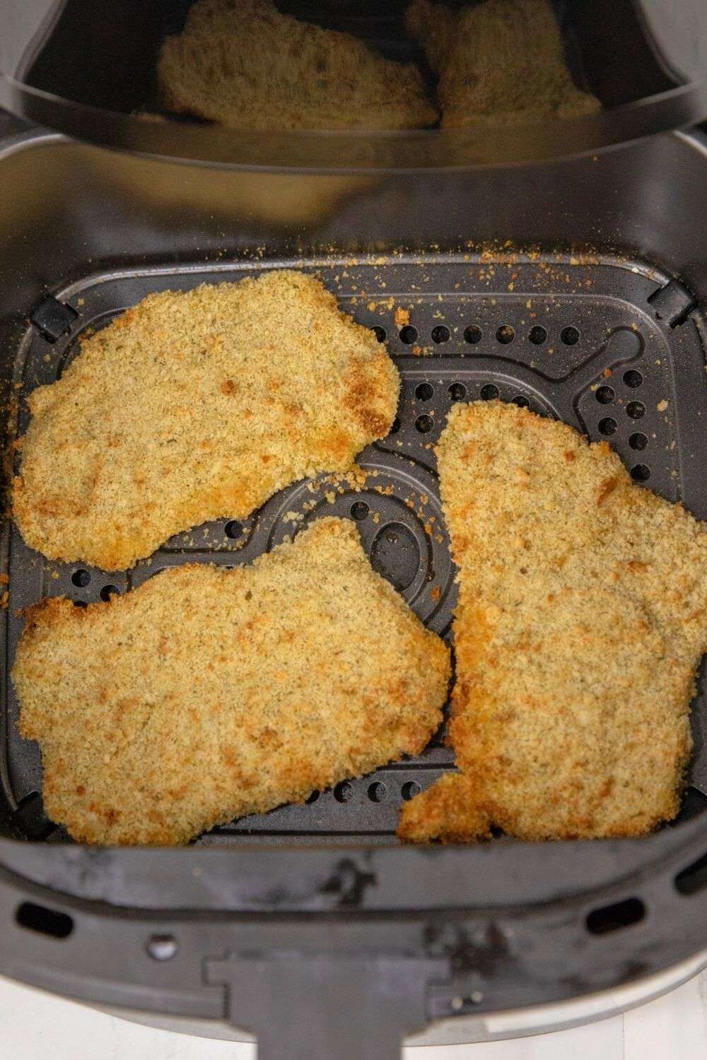 Breaded pork cutlets in air fryer basket.