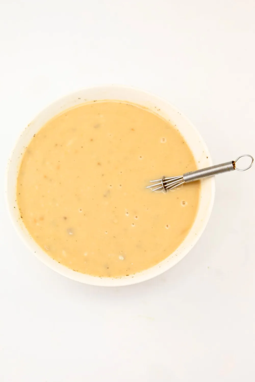 White bowl with wire whisk combining ingredients for crock pot gravy.