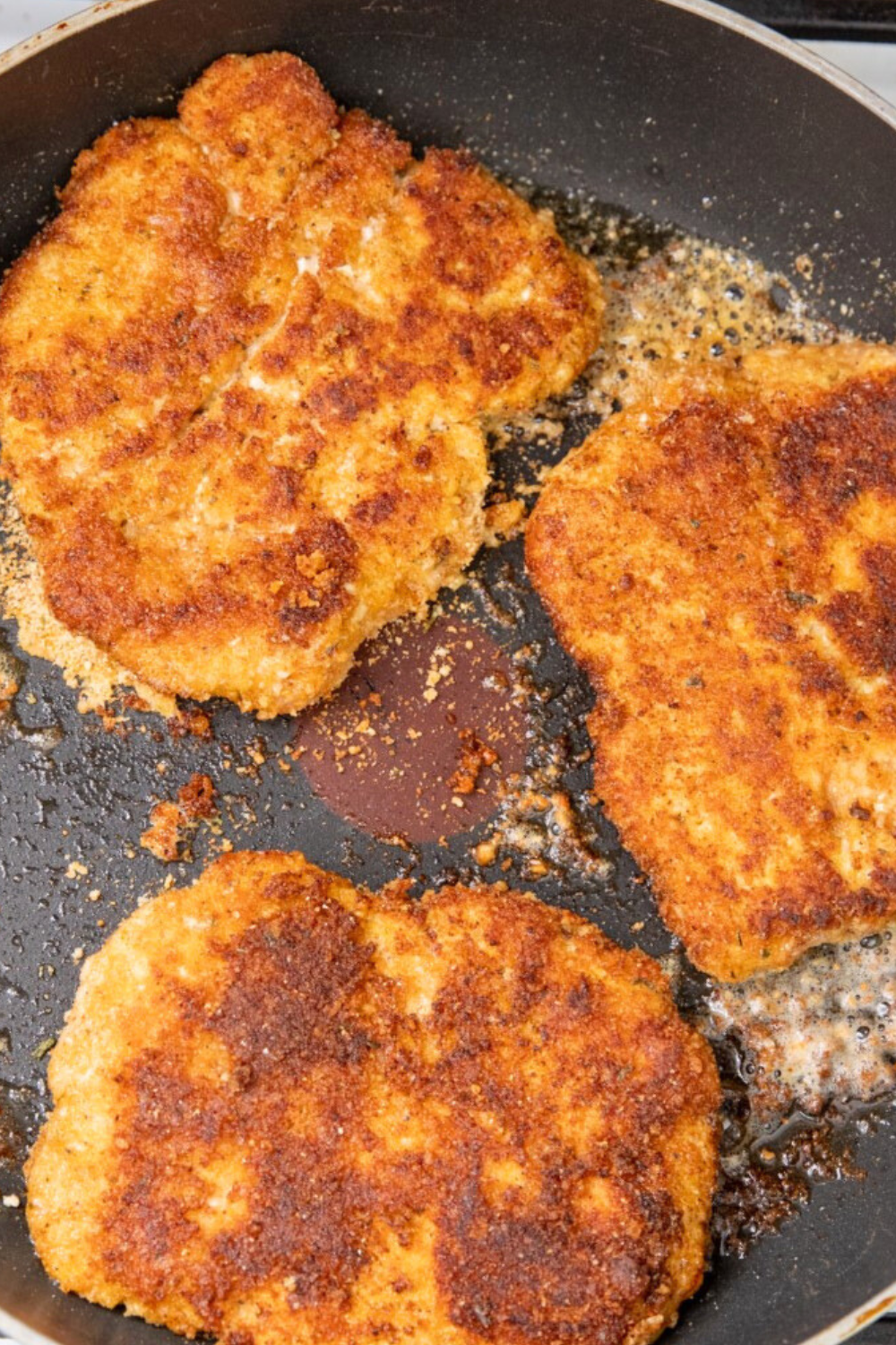 Golden brown breaded pork cube steaks frying in black pan.