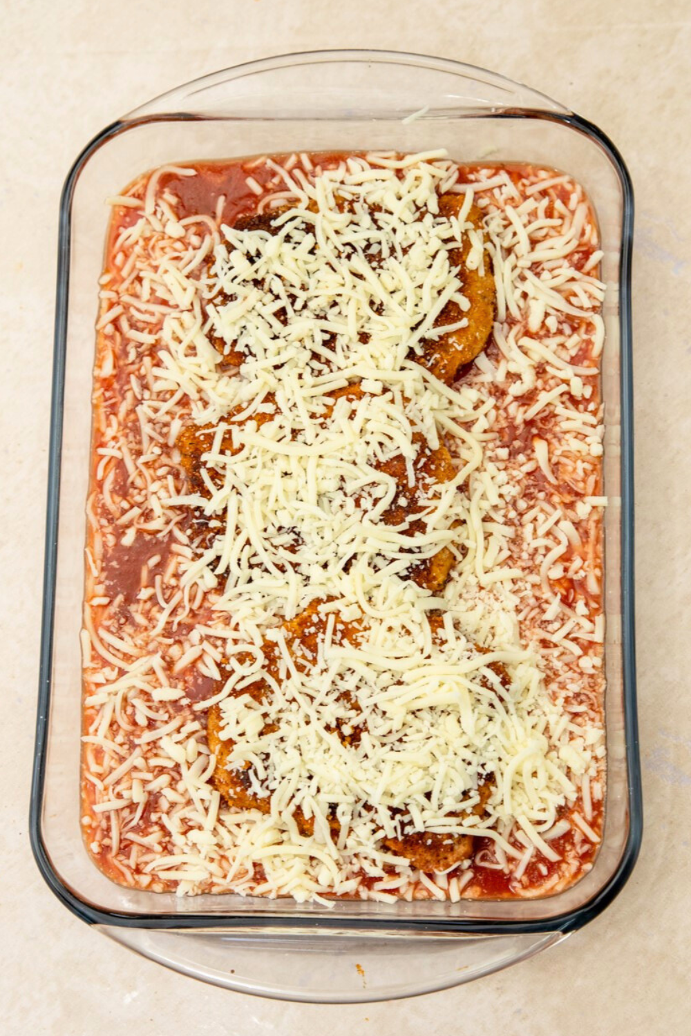 Glass baking dish filled with tomato sauce, pork cube steak parmesan and topped with mozzarella cheese.