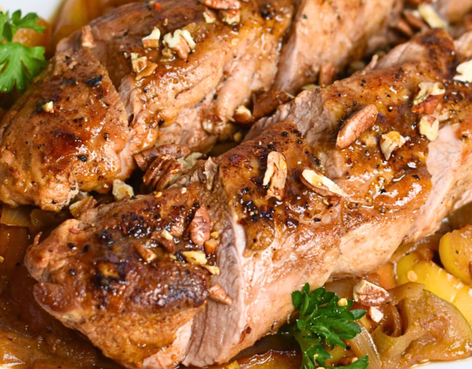 Upclose photo of pork tenderloin with apples and onions topped with toasted pecans.